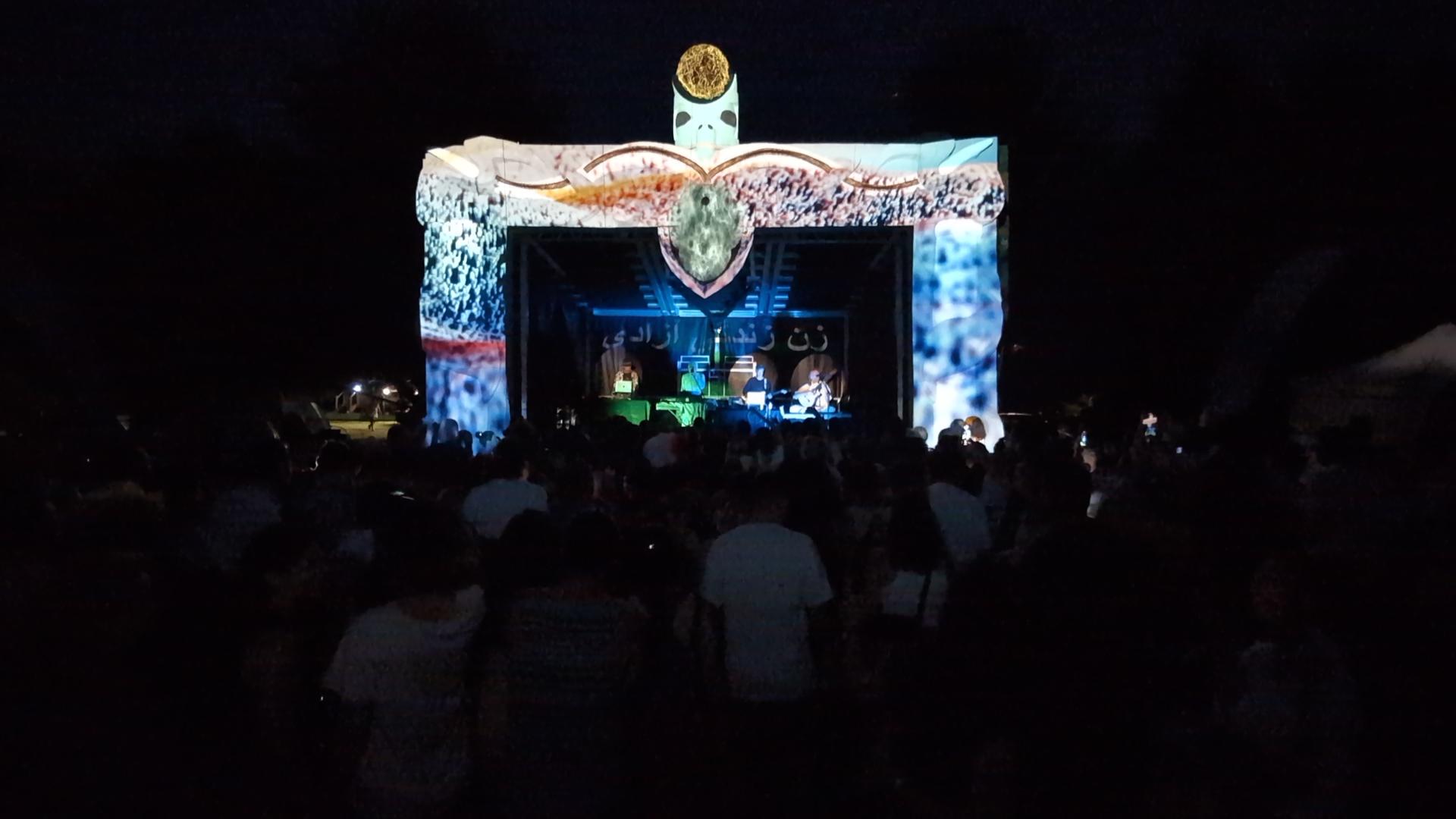 Bumi Festival main stage with full projection mapping of a bird totem design, audience silhouettes in foreground
