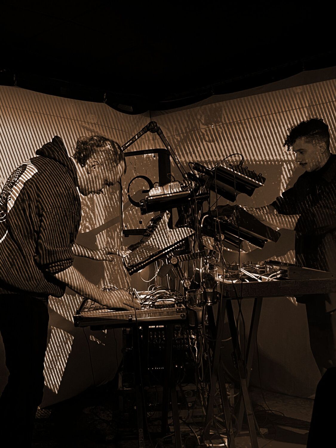 Two electronic musicians with modular synths in front of striped projection-mapped backdrop at Frequencies night